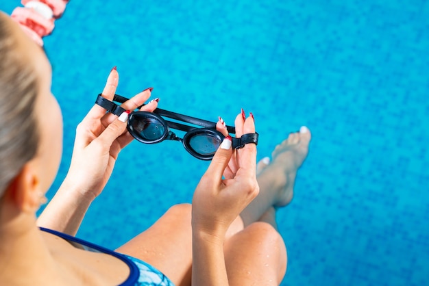 Junge Frau im Schwimmbad, das Schutzbrillen hält, die bereit sind zu schwimmen