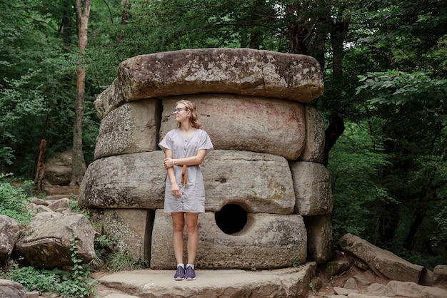 Junge Frau im Sommerkleid, die in der Nähe eines großen Dolmensteins im Wald spaziert