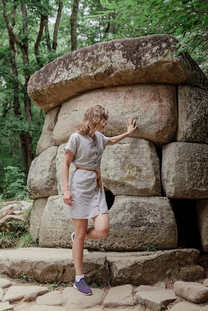 Junge Frau im Sommerkleid, die in der Nähe eines großen Dolmensteins im Wald spaziert