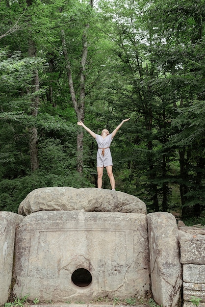 Junge Frau im Sommerkleid steht auf einem großen Felsen im Wald