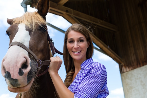 Junge Frau im Stall mit Pferd am Sonnenschein