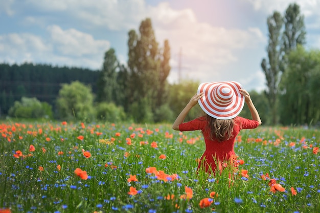 Junge Frau im Strohhut auf Mohnblumenblumenfeld, Sommersaison