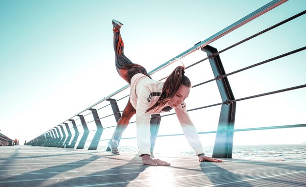 Junge Frau im Trainingsanzug führt Sporttraining auf dem Pier durch