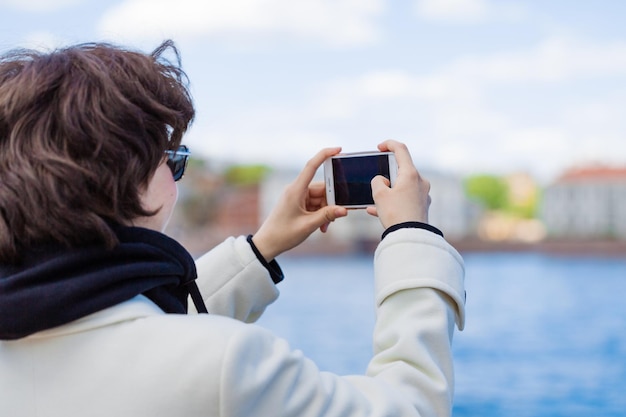 Junge Frau im Urlaub mit Handy, um Fluss und Stadt zu fotografieren