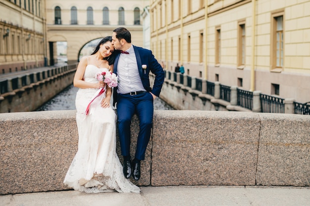 Junge Frau im weißen Hochzeitskleid empfängt Kuss vom Ehemann