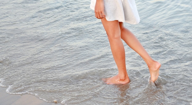 Junge Frau im weißen Kleid allein zu Fuß am Strand.