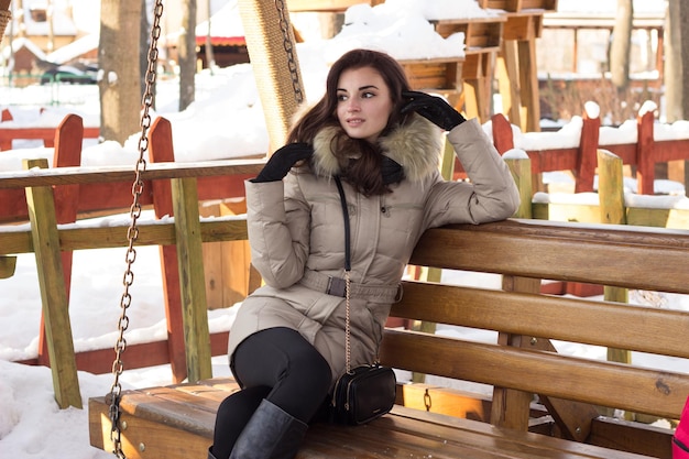 Junge Frau im Winterpark sitzt auf einer Bank mit viel Schnee herum