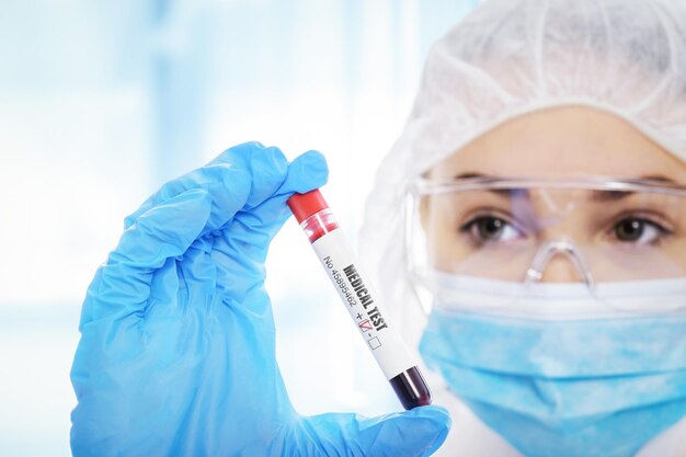 Junge Frau in Arbeitsschutzkleidung testet Blutprobenröhrchen im medizinischen Labor