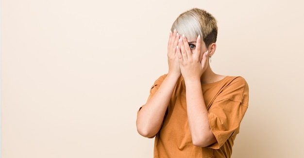 Junge Frau in Übergröße mit kurzen Haaren blinzelt verängstigt und nervös durch die Finger.