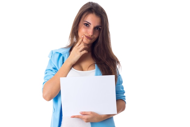 Junge Frau in blauer Jacke und Jeans mit weißem Blatt Papier auf weißem Hintergrund im Studio