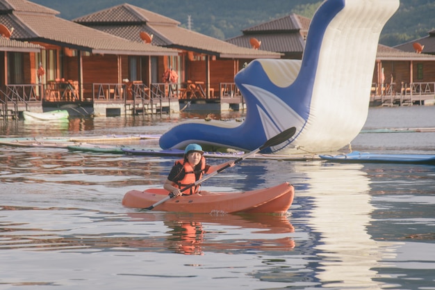 Junge Frau in den orange Schwimmwesten, die auf einem See Kayak fahren. Glückliche junge Frau, die im waterpark canoeing ist