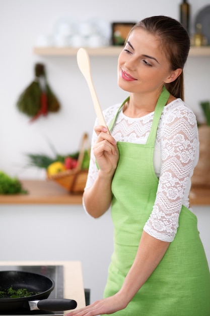 Junge Frau in der grünen Schürze kocht in der Küche Hausfrau denkt über das Menü nach, während sie einen Holzlöffel in der Hand hält