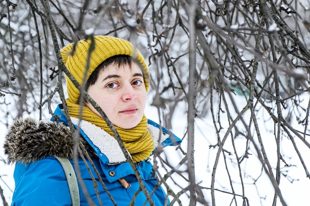 Junge Frau in der hellen Wintermütze und -jacke unter den Zweigen der Bäume im Winterpark.