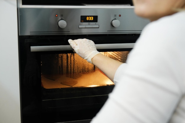 Junge Frau in der Küche kocht Essen im Ofen Das Licht des Ofens prüft die Bereitschaft des Gebäcks