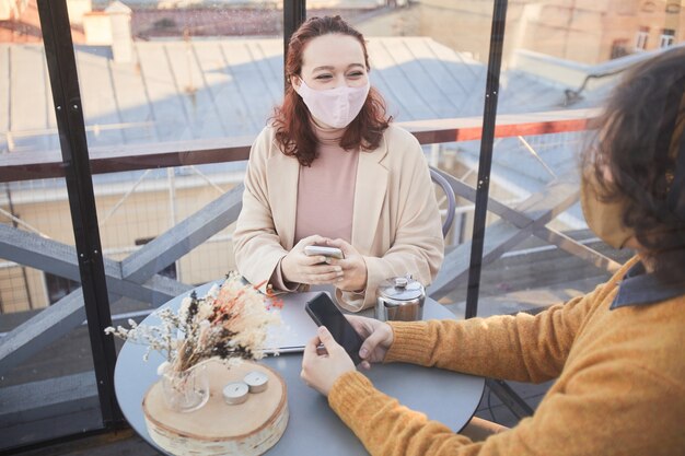 Junge Frau in der Maske, die mit jungem Mann spricht, während sie am Tisch während des Treffens im Restaurant sitzen