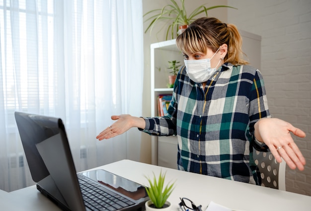 Junge Frau in der medizinischen Maske, die Büroarbeit von zu Hause aus arbeitet