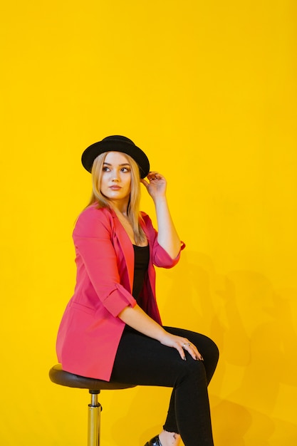 Junge Frau in der rosa Jacke, die auf Stuhl auf Gelb sitzt