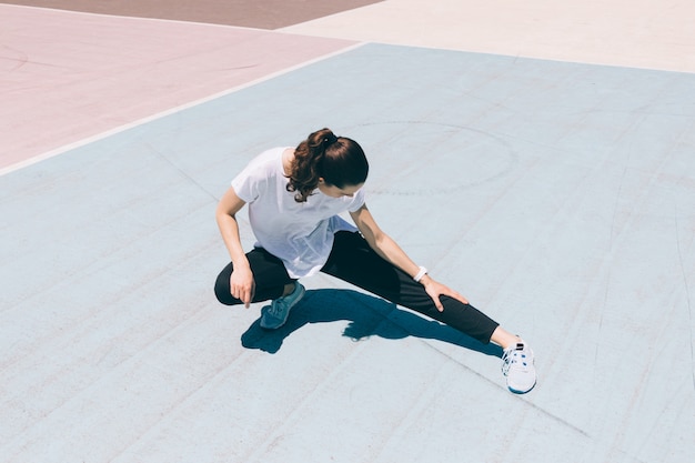 Junge Frau in der Sportkleidung, die Bein auf dem Spielplatz ausdehnend tut