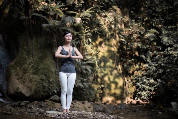 Junge Frau in der Yogahaltung, die nahe Wasserfall archiviert