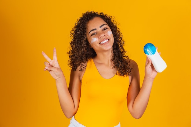 Junge Frau in einem Badeanzug mit Sonnencreme. Junge afro-frau, die sonnencreme aufsetzt, um sich vor der sonne zu schützen