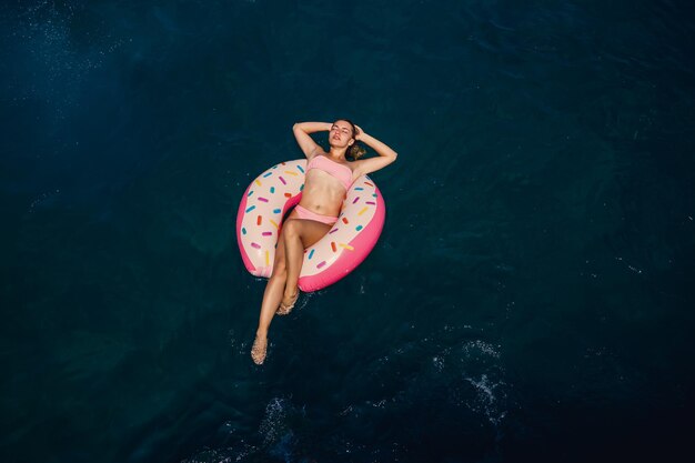 Junge Frau in einem Badeanzug schwimmt auf einem aufblasbaren Ring im Meer Sommerurlaubskonzept