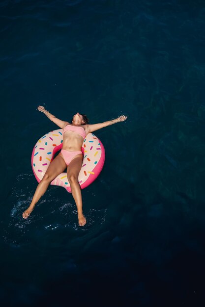 Junge Frau in einem Badeanzug schwimmt auf einem aufblasbaren Ring im Meer Sommerurlaubskonzept