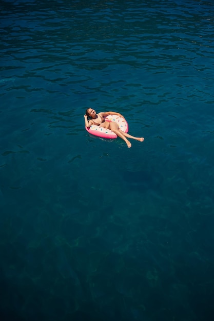 Junge Frau in einem Badeanzug schwimmt auf einem aufblasbaren Ring im Meer Sommerurlaubskonzept