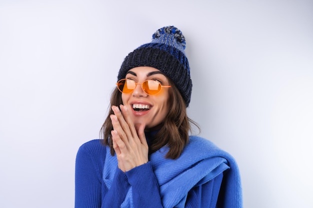 Junge Frau in einem blauen Golfrollkragenhut und in einer Schalsonnenbrille auf einem weißen Hintergrund fröhlich in einer guten Laune