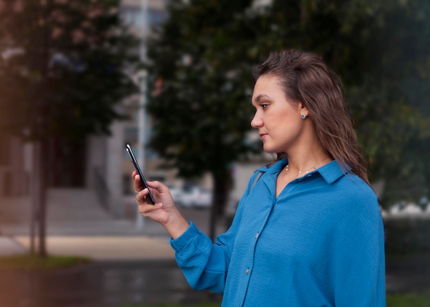 Junge Frau in einem blauen Hemd mit einem Mobiltelefon in der Hand