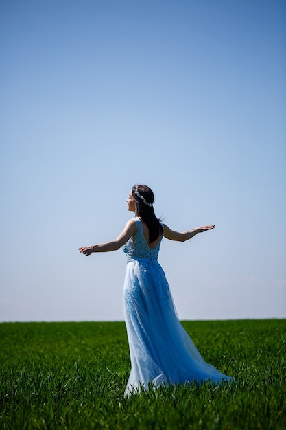 Junge Frau in einem blauen langen Kleid auf einem Hintergrund der grünen Wiese. Modeporträt eines schönen Mädchens mit einem Lächeln im Gesicht