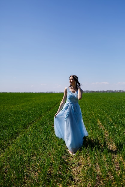 Junge Frau in einem blauen langen Kleid auf einem Hintergrund der grünen Wiese. Modeporträt eines schönen Mädchens mit einem Lächeln im Gesicht