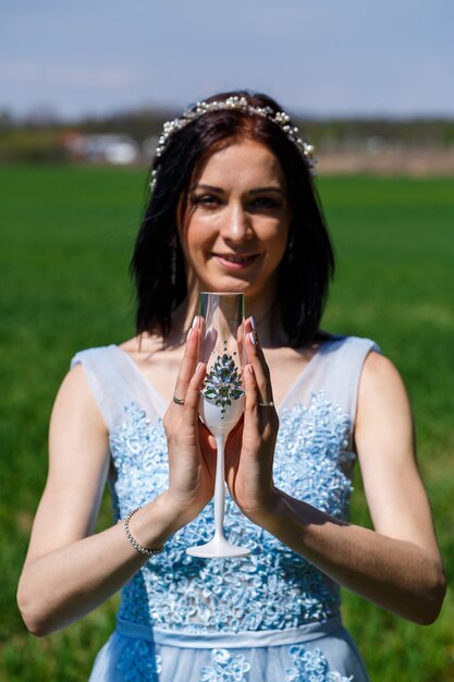 Junge Frau in einem blauen langen Kleid hält ein Glas in den Händen