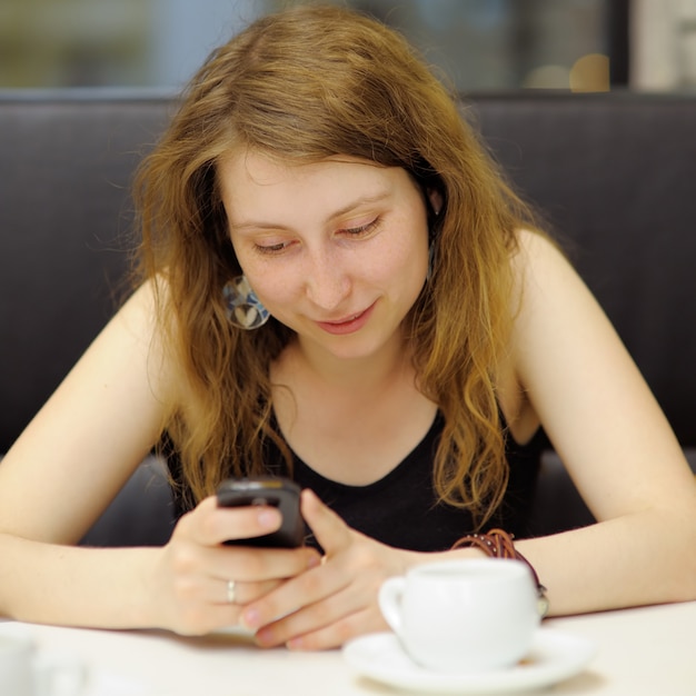 Junge Frau in einem Café unter Verwendung ihres Handys