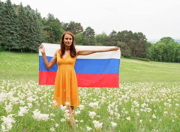 Junge Frau in einem gelben Kleid mit der Nationalflagge Russlands draußen auf einem blühenden Feld