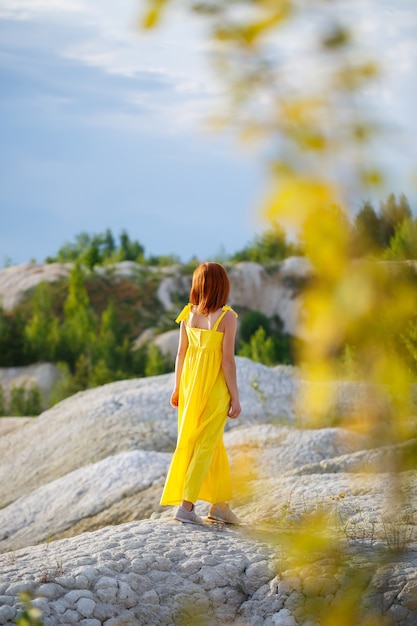 Junge Frau in einem gelben Kleid nahe dem See mit azurblauem Wasser und grünen Bäumen.