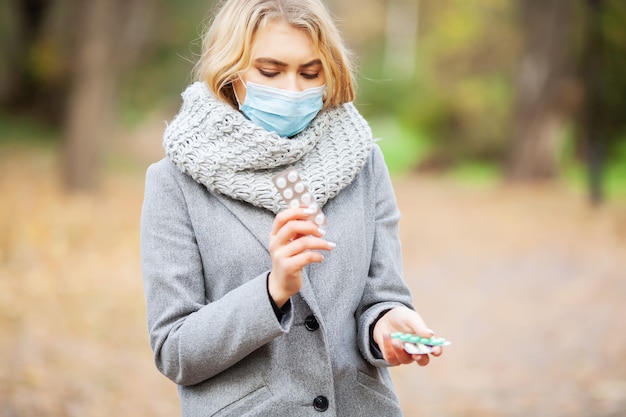 Junge frau in einem grauen mantel gehend in den herbstpark mit einer maske