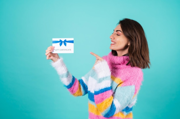 Junge Frau in einem hellen bunten Pullover auf Blau mit einem Geschenkgutschein