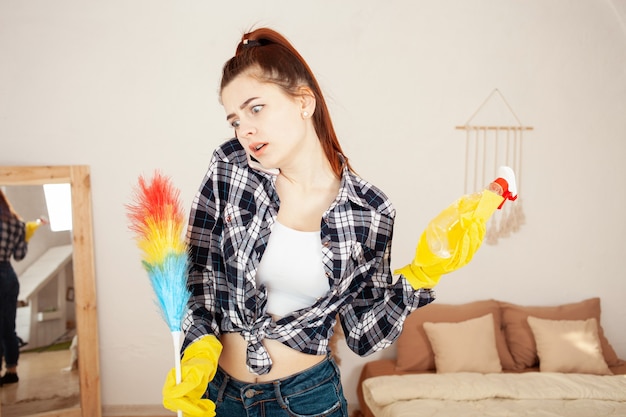 Junge Frau in einem Hemd und Gummihandschuhen, die im Haus putzen und am Telefon sprechen