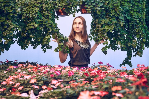 Junge Frau in einem Kleid zwischen dekorativem Grün und Blumen auf hellblauem Hintergrund