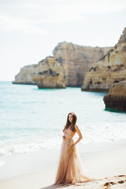 junge Frau in einem langen Kleid, die am Strand in der Nähe des Ozeans spazieren geht.