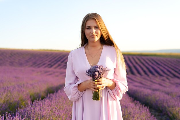 Junge Frau in einem lila Kleid, die in einem Lavendelfeld spaziert