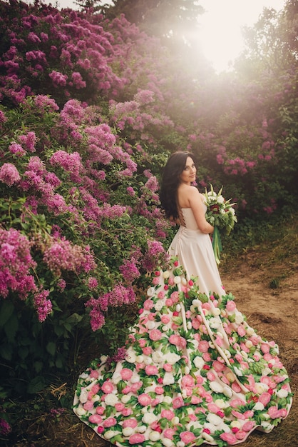 Junge Frau in einem Pfingstrosenkleid steht in einem blühenden lila Garten bei Sonnenuntergang