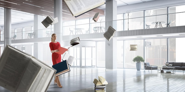 Junge Frau in einem roten Kleid, das ein Buch liest, während andere Bücher herumfliegen. Gemischte Medien