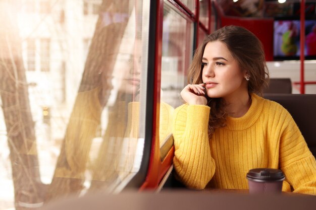 Junge Frau in einem Senfpullover sitzt in einem Café und schaut aus dem Fenster