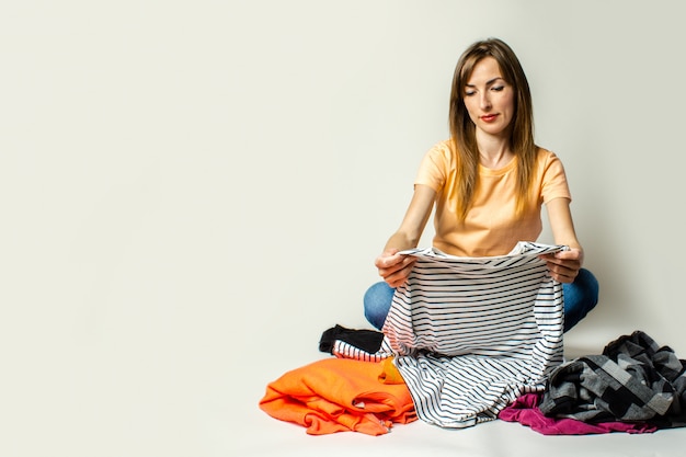 Foto junge frau in einem t-shirt und in jeans wählt dinge, während auf dem boden auf einem hellen hintergrund sitzend