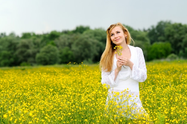 Junge Frau in einem weißen Spitzenkleid, das mit Blumen in ihren Händen aufwirft