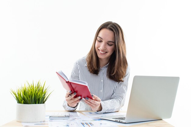 Junge Frau in einer Büro-Kleiderordnung sitzt an ihrem Schreibtisch und macht sich Notizen