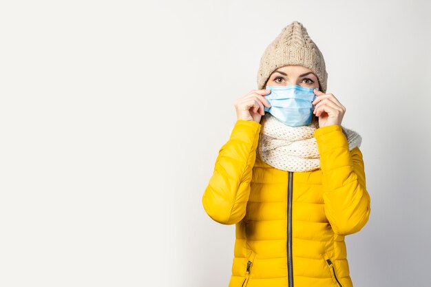 Junge Frau in einer gelben Jacke und einem Hut mit einer medizinischen Maske