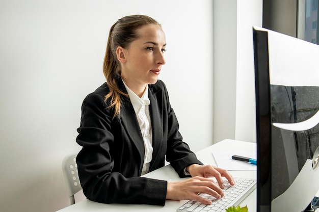 Junge Frau in einer Jacke, die an einem Computer am Arbeitsplatz sitzt