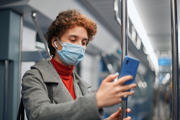 Junge Frau in einer Schutzmaske, die ein Selfie macht, während sie in einem U-Bahn-Wagen steht